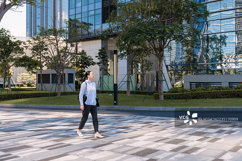 一位亚洲女商人在户外散步，背景是摩天大楼图片素材