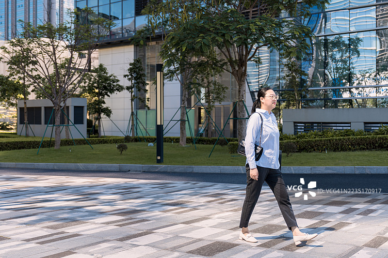 一位亚洲女商人正在户外散步，背景是摩天大楼图片素材