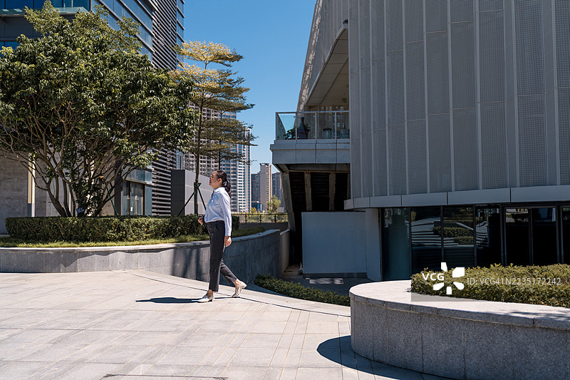一位亚洲女商人正在户外散步，背景是摩天大楼。图片素材