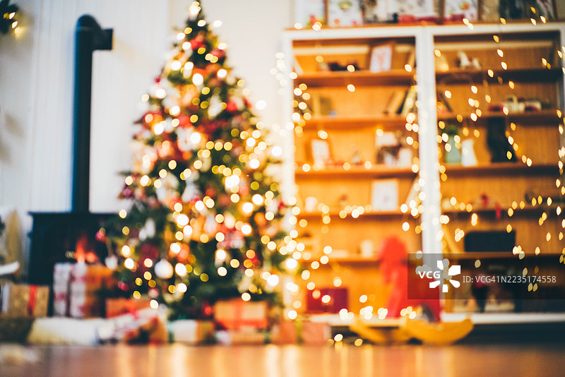 装饰精美的节日房间，有圣诞树、壁炉和扶手椅。圣诞新年室内：壁炉、灯具、圣诞树、礼物和许多闪烁的灯光。图片素材