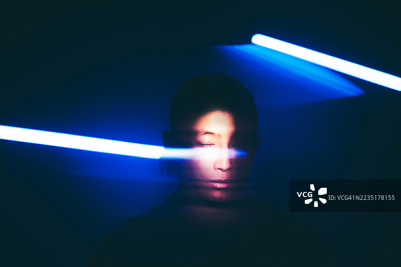 一位亚洲男子的肖像，闭着眼睛，脸部部分被明亮的蓝色光条遮挡。图片素材
