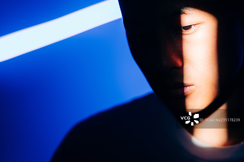 一束光线将人物的面部肖像戏剧性地分割成明暗两部分，背景是醒目的蓝色光芒。图片素材