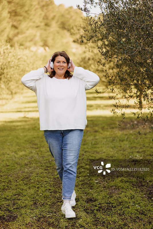 快乐的女人在大自然中触摸耳机，安静地聆听。图片素材