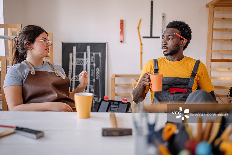 年轻人在木工车间开始小生意，休息时喝咖啡聊天放松。图片素材