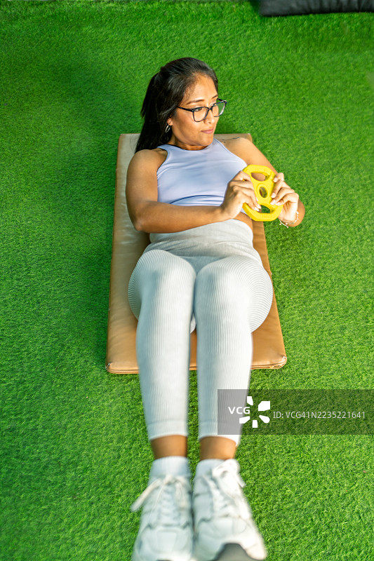 年轻女性在健身垫上进行负重腹部卷曲练习图片素材