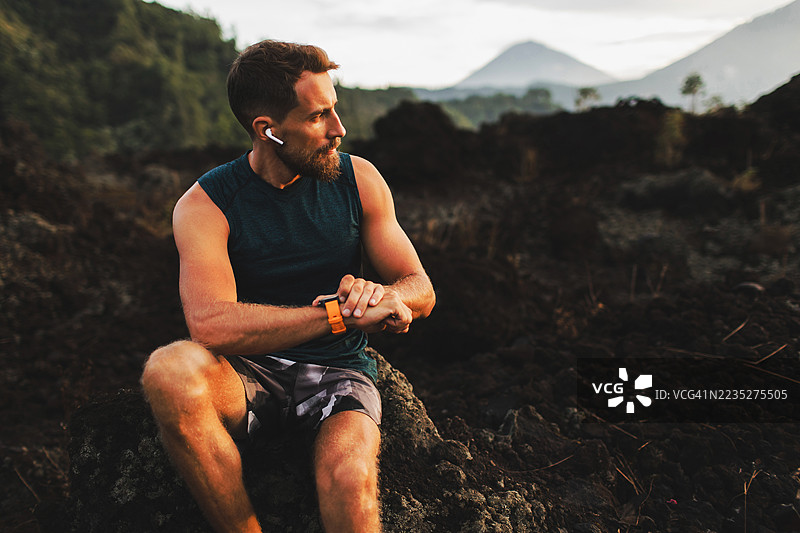 年轻的时尚跑者，留着胡须，使用智能手表并听音乐图片素材