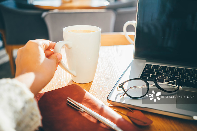 一位女士在喝咖啡休息时使用笔记本电脑，特写她的双手图片素材