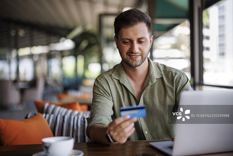 男子在咖啡馆使用笔记本电脑和信用卡进行在线购物图片素材