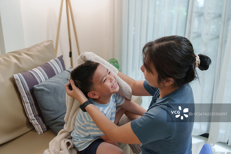 亚洲母亲在儿子洗澡后，轻轻地为他擦去头发上的水珠。图片素材