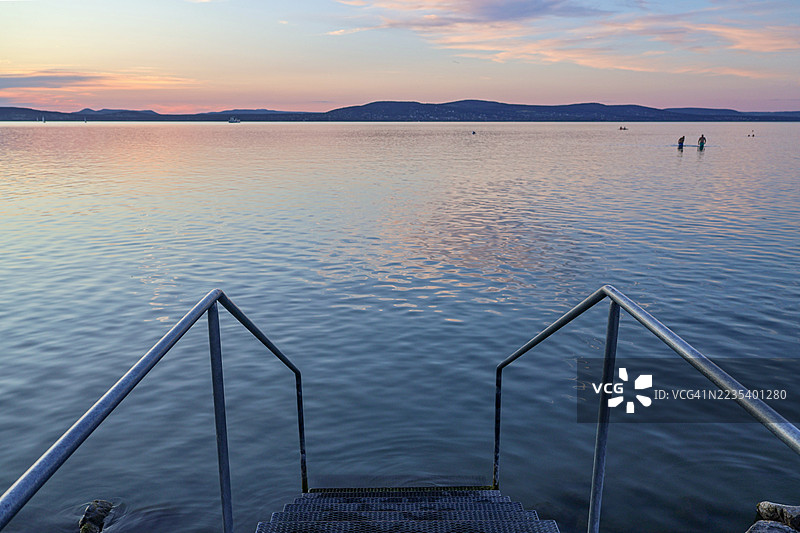 从巴拉顿湖海滩岸边，沿着伸入水中的台阶望去，柔和色调的日落景象图片素材
