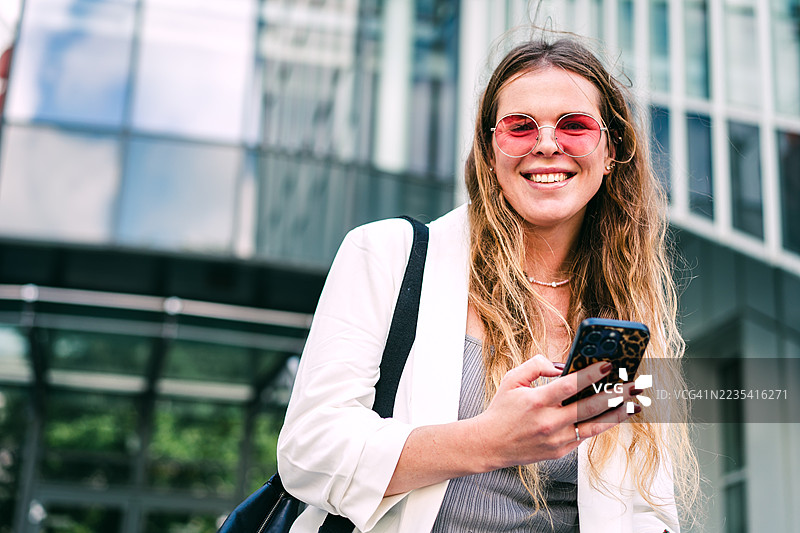 微笑的年轻女性在城市商业区户外使用智能手机图片素材