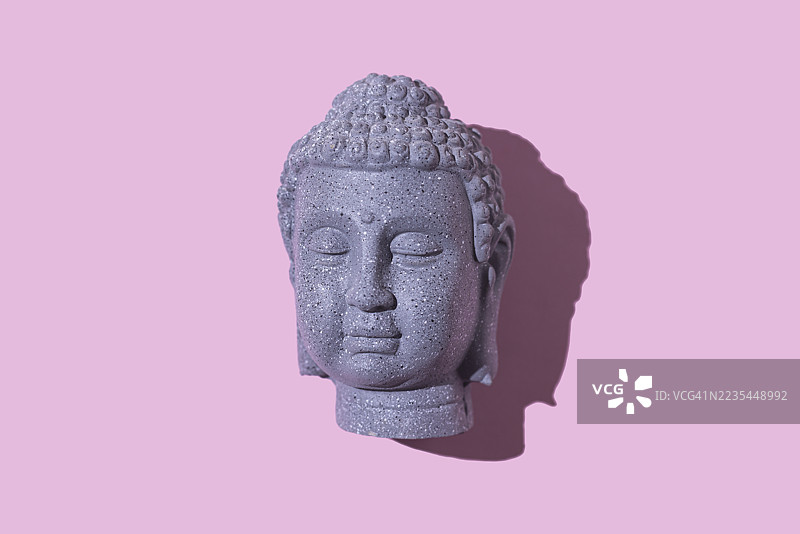 粉色背景上的灰色石头佛像头。佛教，灵性，禅，神，信仰，和平，宁静，印度和泰国。图片素材