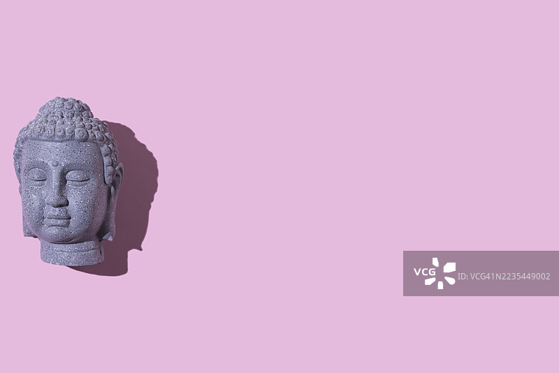 灰色石头佛像头部，位于左侧，背景为粉色。佛教，灵性，禅，神，信仰，和平，宁静，印度和泰国。图片素材
