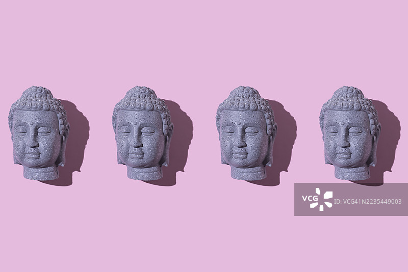 灰色石佛像头部的排列，背景为粉色。佛教，灵性，禅，神，信仰，和平，宁静，印度和泰国。图片素材