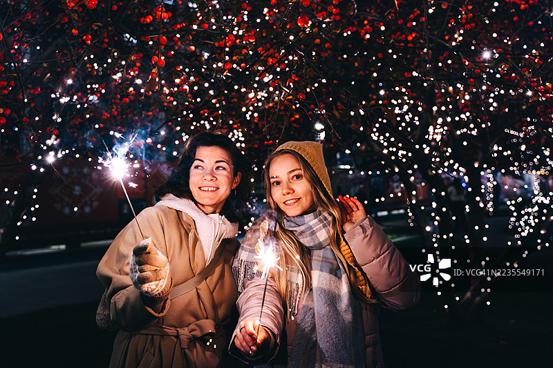 两个年轻女性快乐地仰望着，手中拿着烟花棒。图片素材