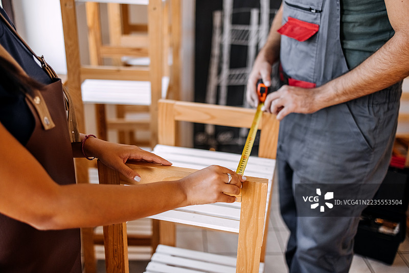年轻人在他们的小型家庭木工车间制作木制品，并检查制作的架子的尺寸图片素材