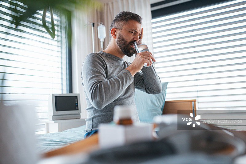 男子坐在医院病床上，感到剧烈的疼痛和头痛。图片素材
