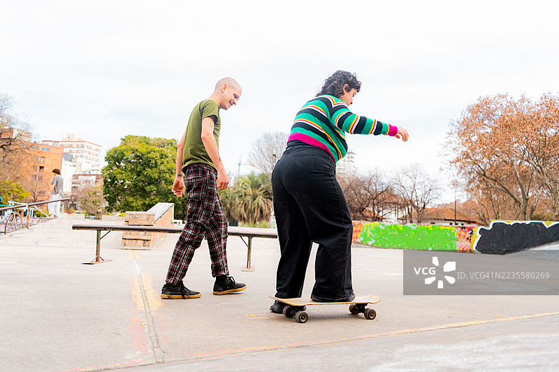 中年男子在公园的跑道上教朋友滑滑板图片素材