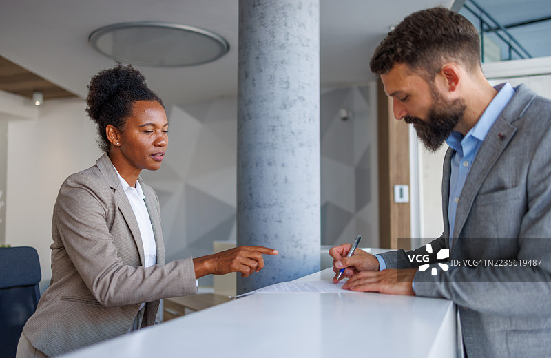 商人在现代办公室签署合同，接待员协助。图片素材