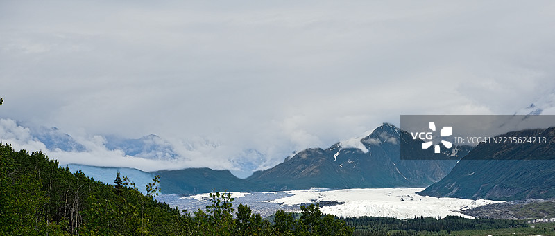 雄伟的山脉下有一片广阔的冰川，天空布满云彩图片素材