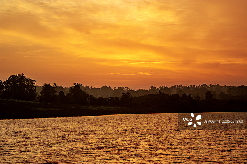 金色时光映照在宁静的湖面上，树木的剪影与鲜艳的橙色和黄色天空相映成趣，爱尔兰卡范图片素材