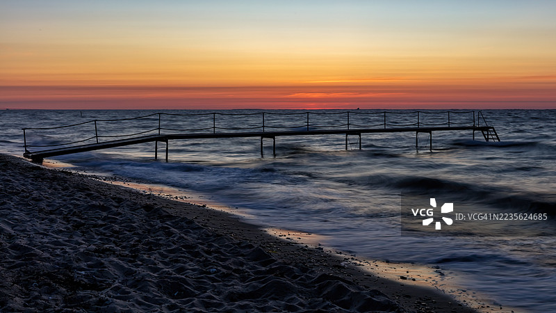丹麦朗厄兰岛的码头和海洋上宁静的日落，海浪拍打着沙滩图片素材