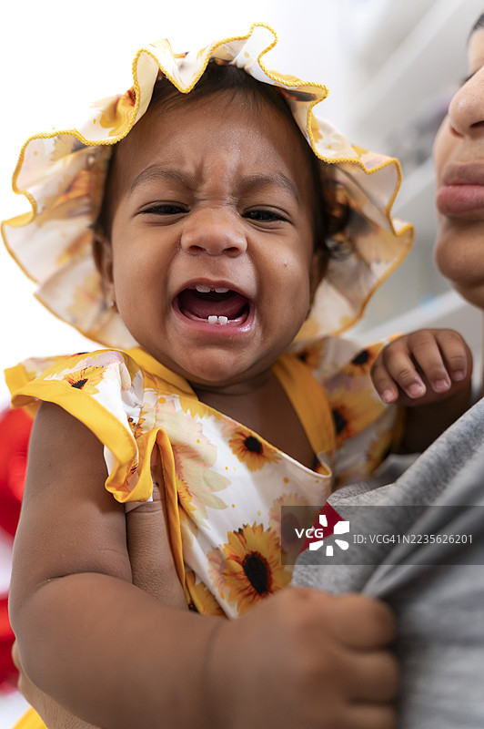 母亲怀中哭泣的婴儿女孩露出第一颗牙齿图片素材