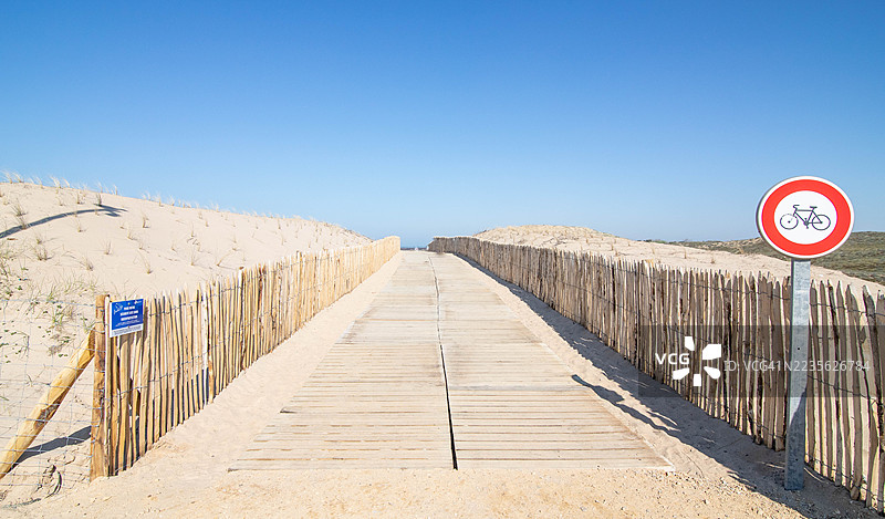 阳光明媚的日子里，木栈道穿过沙丘通向大海，法国图片素材