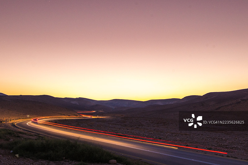 傍晚时分，在以色列阿拉德蜿蜒的沙漠公路上，汽车灯光轨迹的长曝光照片图片素材