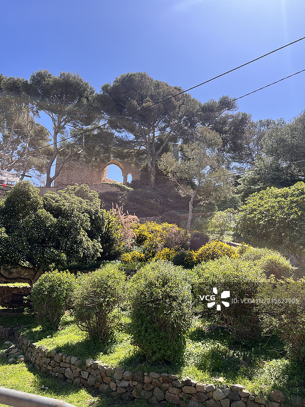 郁郁葱葱的花园与历史悠久的石头遗迹在晴朗的蓝天下，西班牙托萨德马尔图片素材