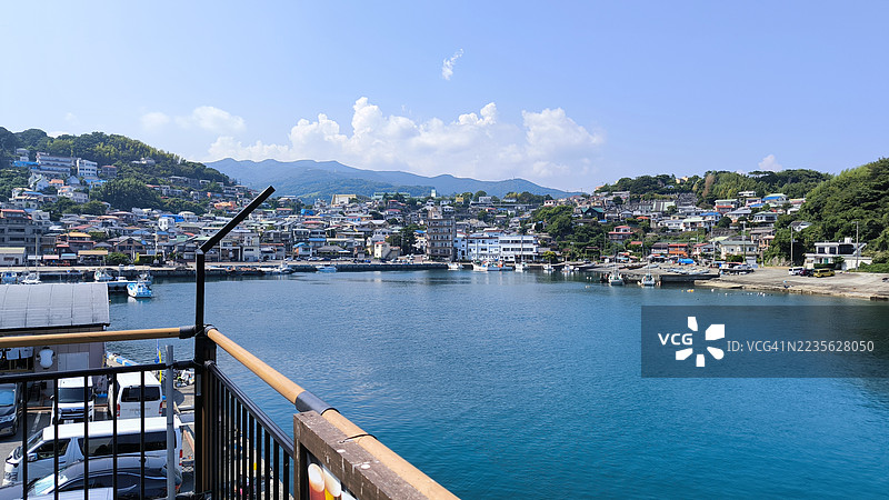 风景如画的海滨小镇，港口坐落在绿丘之间，蓝天清澈，位于日本图片素材