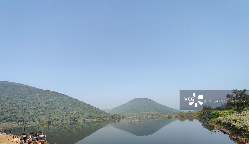 宁静的湖泊景观，倒映着郁郁葱葱的绿色山脉和晴朗的蓝天，印度卡塔克图片素材
