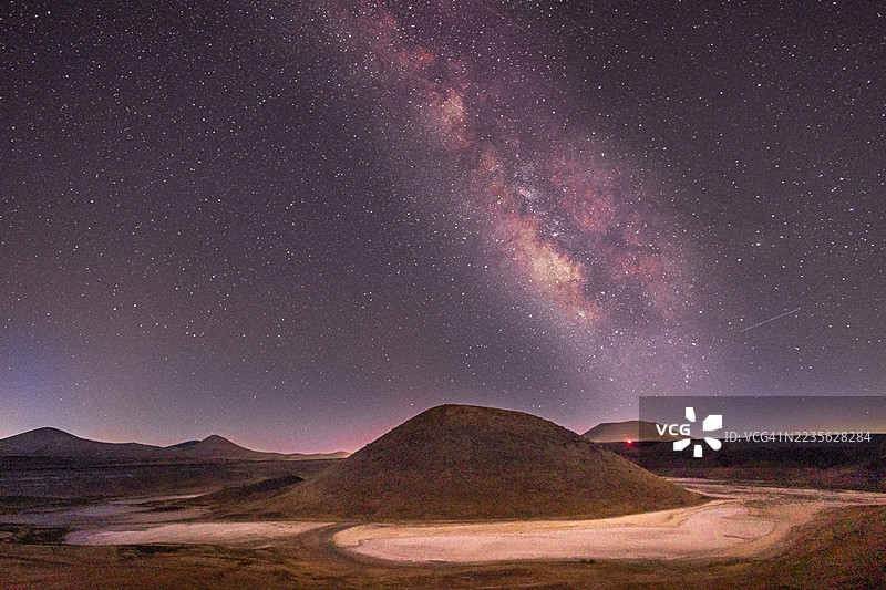 壮观的银河系拱形横跨夜晚的火山丘陵图片素材