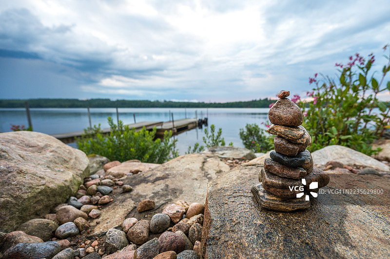 宁静湖边堆叠石头的特写，背景是戏剧性的天空，象征着平衡与宁静，瑞典图片素材
