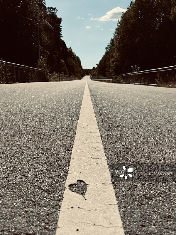 蓝天下，一条空旷道路的白色线条上有一个心形裂缝，延伸向远方。图片素材