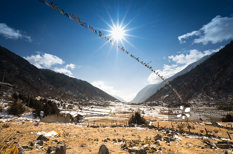 阳光明媚，照耀着广阔的山谷，山谷中飘扬着祈祷旗，隐约可见雪迹，印度图片素材