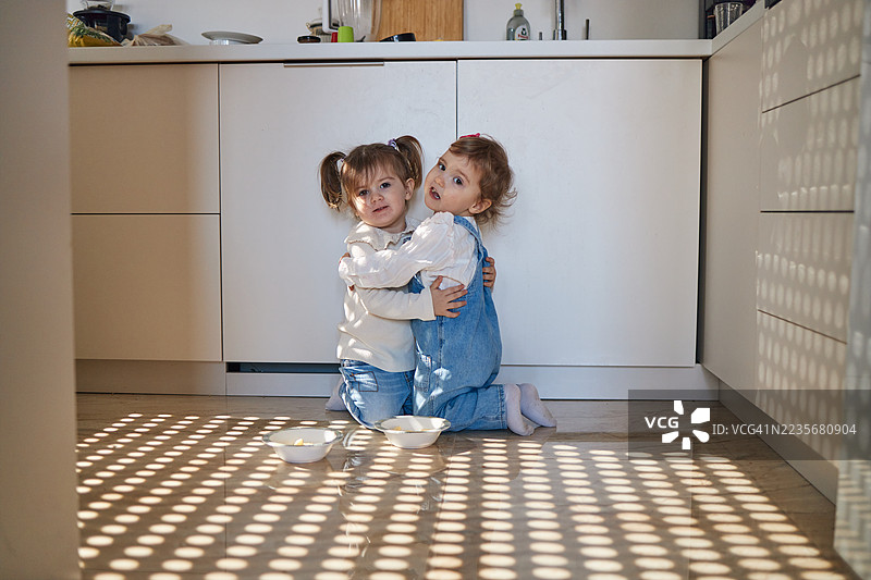 漂亮的双胞胎女孩在厨房地板上玩耍并吃东西图片素材