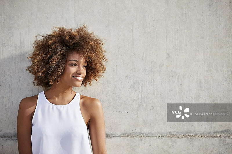 快乐的年轻女性穿着背心靠在墙上图片素材