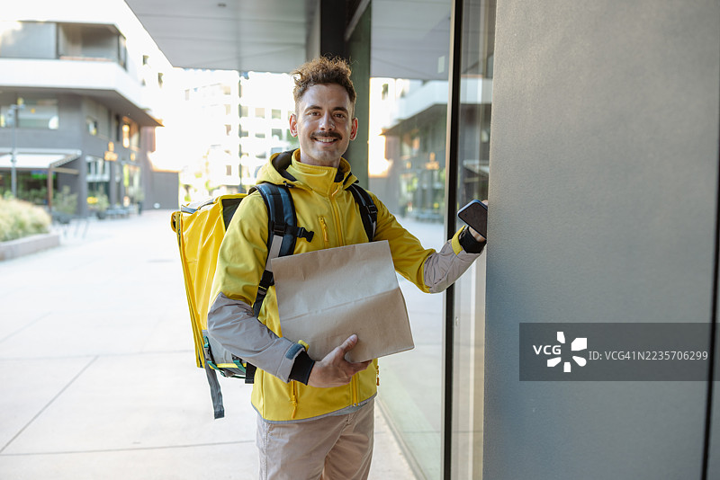 微笑的快递员在现代建筑外手持包裹的肖像图片素材