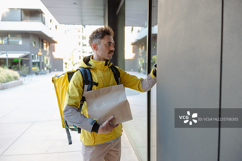 送货服务员敲门，手里拿着包裹和黄色背包图片素材