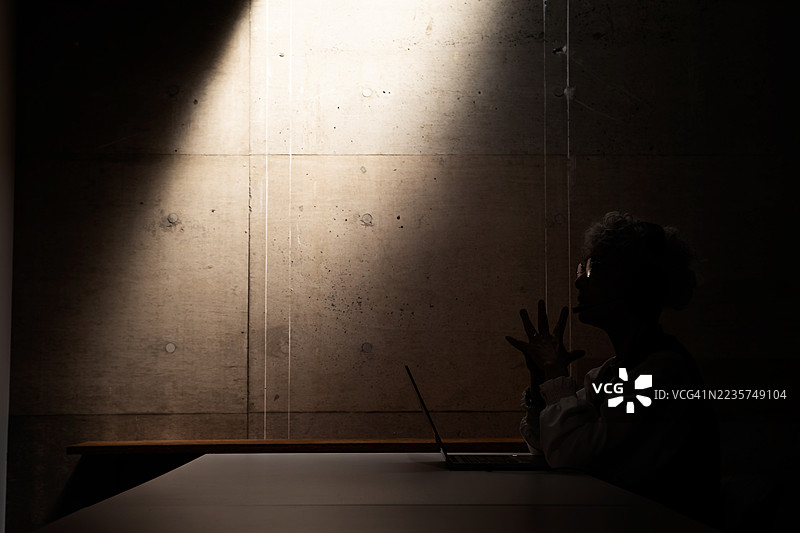 一位年长的女性在灯光熄灭的黑暗房间里参加在线会议。图片素材