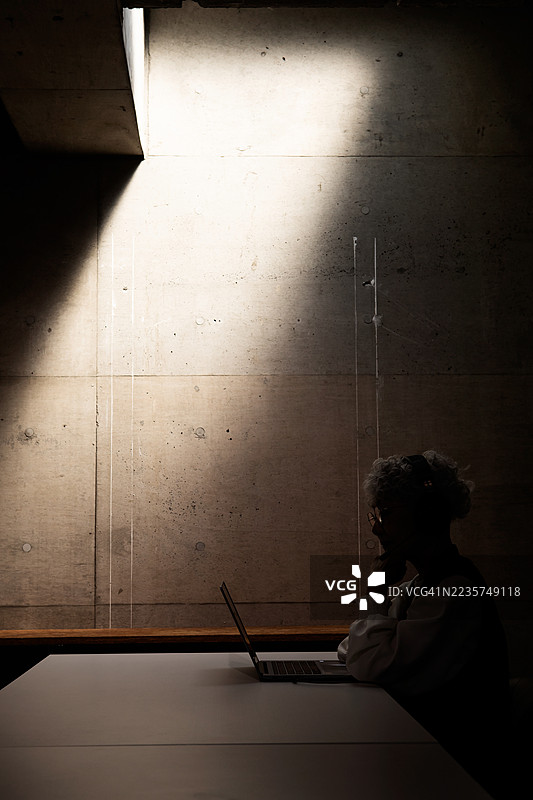 一位年长的女性在灯光熄灭的黑暗房间里进行在线会议。图片素材