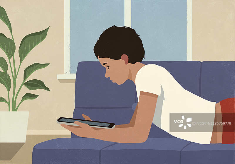 男孩在家放松，躺在客厅沙发上使用平板电脑图片素材