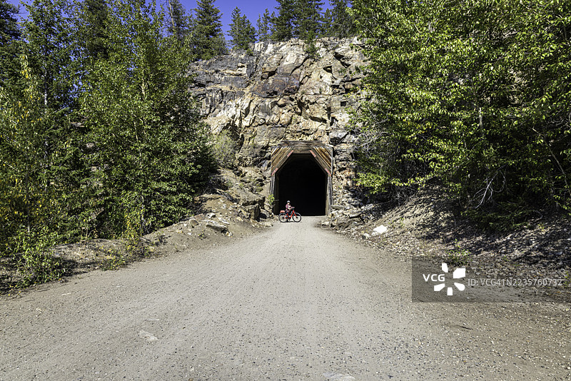 骑自行车的人在加拿大不列颠哥伦比亚省基洛纳的迈拉峡谷小径一个岩石隧道的入口处摆姿势图片素材