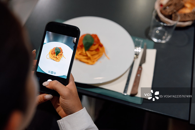 女人在餐厅拍摄一盘素食意大利面的照片图片素材