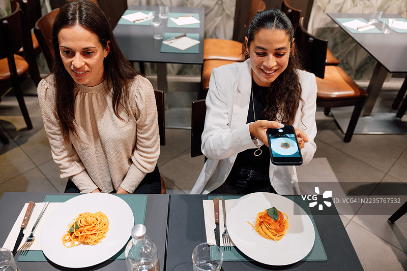 女性在餐厅拍摄素食意大利面的照片图片素材