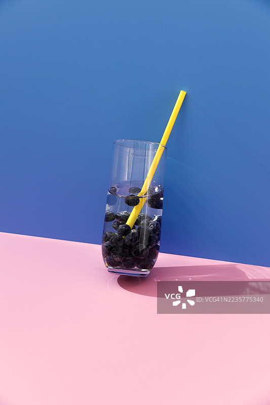 蓝粉色背景下的蓝莓水杯和黄色吸管图片素材