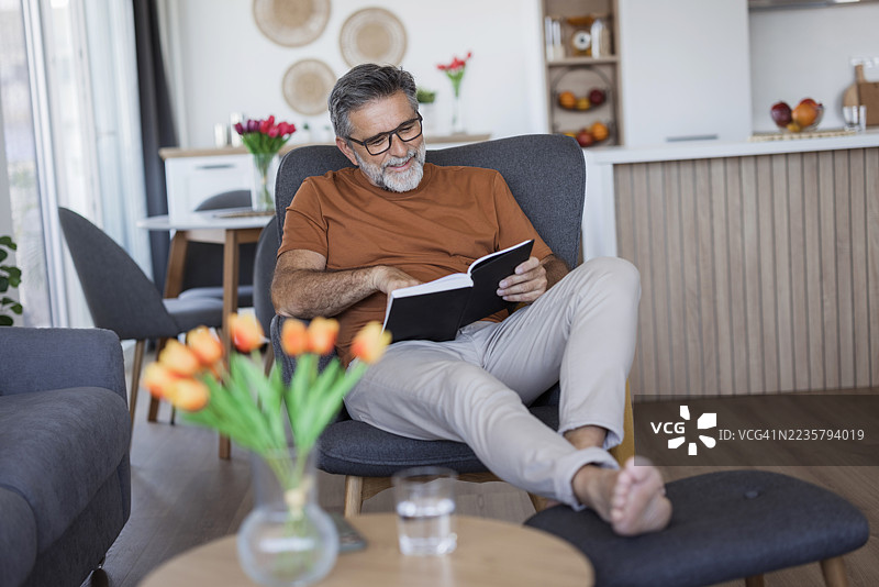 一位成熟的男士在家里的扶手椅上放松地阅读书籍图片素材