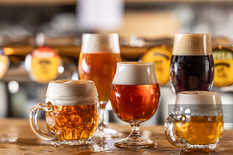 几种不同类型和颜色的生啤酒，盛在不同的酒杯中，摆放在酒吧的木质吧台上。图片素材
