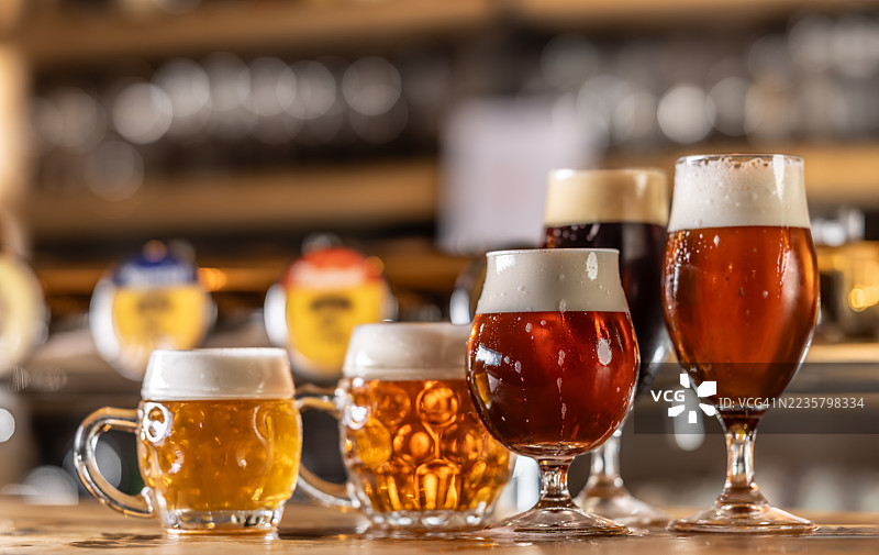 几种不同类型和颜色的生啤酒，盛在不同的酒杯中，摆放在酒吧的木质吧台上。图片素材